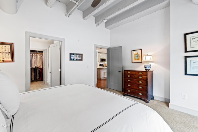 carpeted bedroom with ceiling fan, beam ceiling, a spacious closet, a high ceiling, and a closet