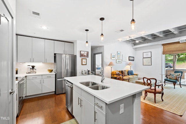 kitchen with backsplash, stainless steel appliances, sink, decorative light fixtures, and an island with sink