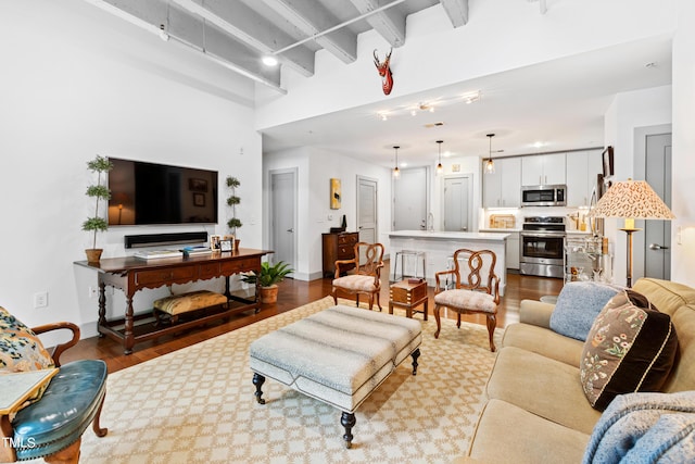 living room with beamed ceiling, a high ceiling, rail lighting, and hardwood / wood-style flooring