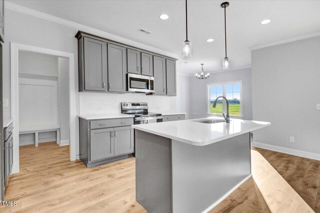 kitchen featuring pendant lighting, sink, crown molding, appliances with stainless steel finishes, and an island with sink