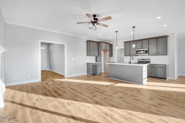 kitchen featuring appliances with stainless steel finishes, hanging light fixtures, ornamental molding, a kitchen island with sink, and light wood-type flooring