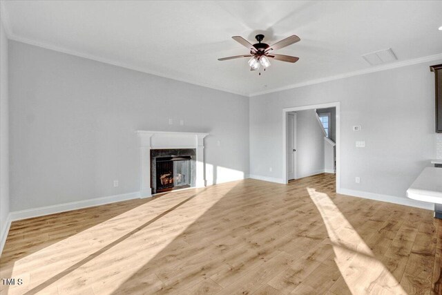 unfurnished living room with crown molding, a high end fireplace, ceiling fan, and light wood-type flooring