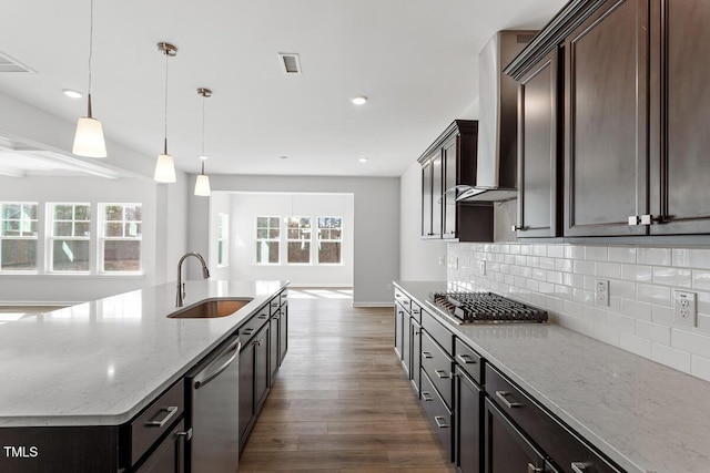 kitchen with tasteful backsplash, wall chimney exhaust hood, wood finished floors, stainless steel appliances, and a sink