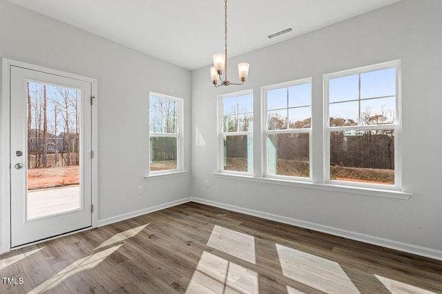 unfurnished dining area with an inviting chandelier, visible vents, baseboards, and wood finished floors