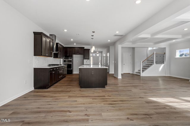 kitchen featuring dark brown cabinetry, open floor plan, light wood-type flooring, decorative backsplash, and wall chimney exhaust hood