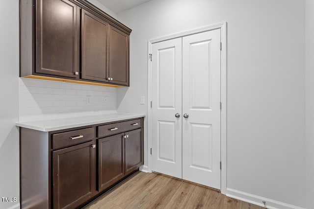 interior space with light countertops, light wood-style flooring, decorative backsplash, dark brown cabinetry, and baseboards