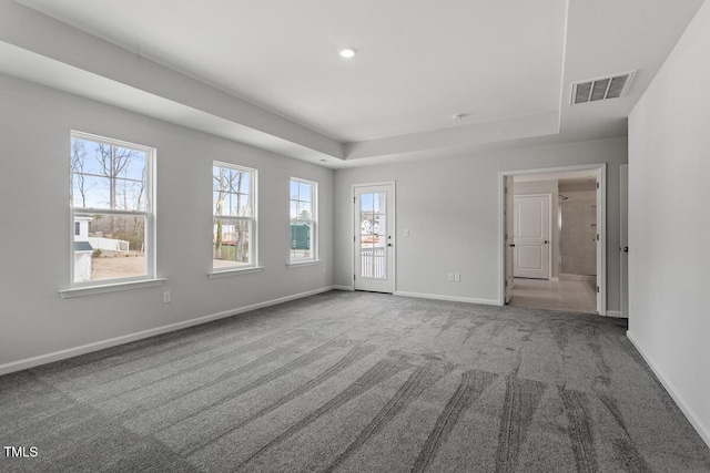 empty room featuring carpet, visible vents, a raised ceiling, and baseboards