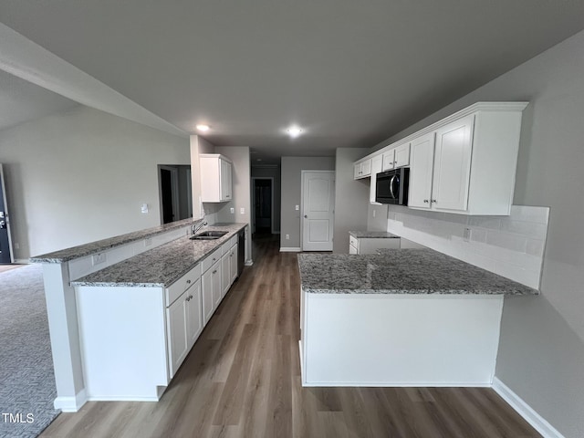 kitchen featuring stainless steel microwave, stone countertops, a peninsula, light wood-style flooring, and a sink