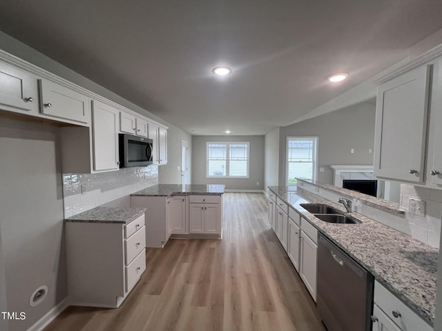 kitchen with light stone counters, appliances with stainless steel finishes, a high end fireplace, light wood finished floors, and a sink