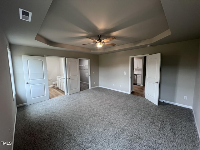 unfurnished bedroom featuring a tray ceiling, baseboards, visible vents, and carpet floors