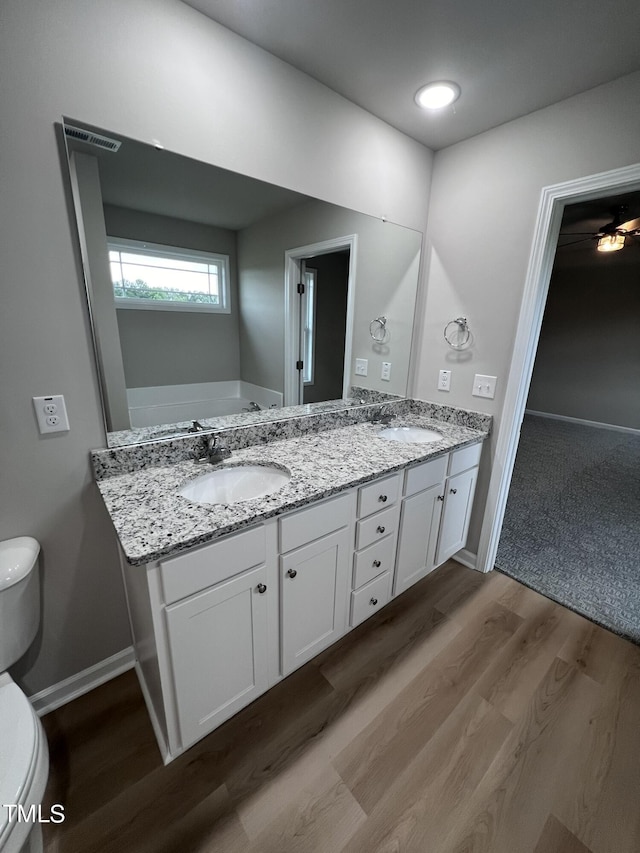 full bath with baseboards, a sink, toilet, double vanity, and wood finished floors