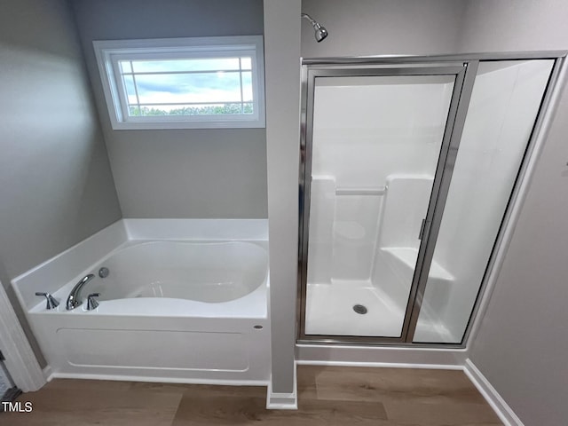 bathroom with a bath, baseboards, a stall shower, and wood finished floors