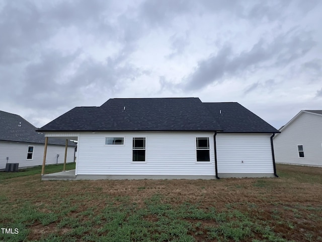 rear view of house with cooling unit, a lawn, and roof with shingles