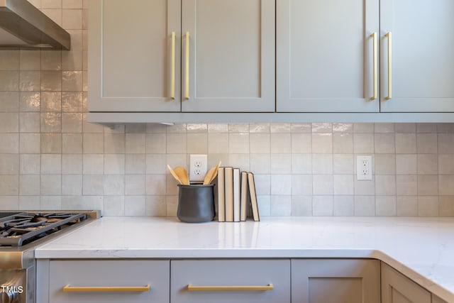 kitchen with tasteful backsplash, wall chimney range hood, light stone counters, and gray cabinets