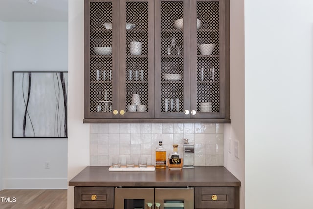 bar with tasteful backsplash, wine cooler, wood-type flooring, and dark brown cabinetry