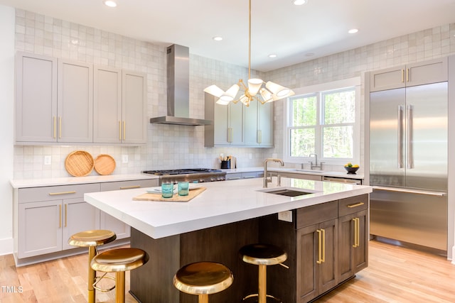 kitchen with appliances with stainless steel finishes, wall chimney exhaust hood, hanging light fixtures, a center island with sink, and a breakfast bar area