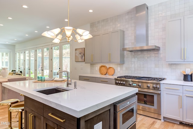 kitchen featuring light stone countertops, appliances with stainless steel finishes, wall chimney exhaust hood, decorative backsplash, and sink