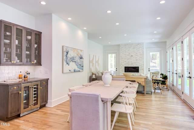 dining room with a fireplace, beverage cooler, a healthy amount of sunlight, and light wood-type flooring