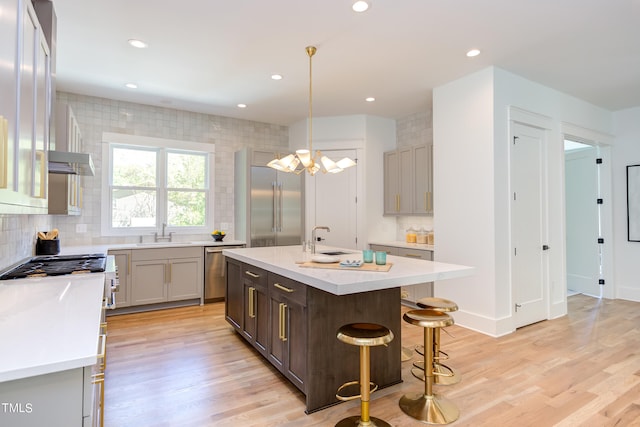 kitchen with pendant lighting, sink, a kitchen island with sink, light wood-type flooring, and a breakfast bar area