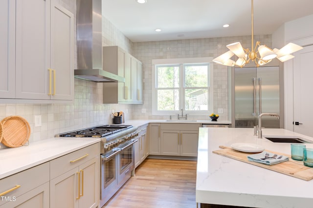 kitchen with an inviting chandelier, decorative light fixtures, high end appliances, wall chimney exhaust hood, and light stone counters