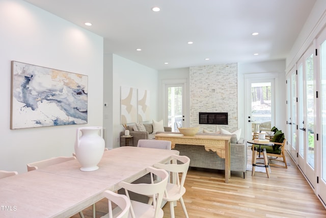 dining room featuring a healthy amount of sunlight, a fireplace, french doors, and light hardwood / wood-style floors