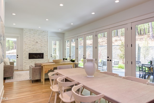 dining area with light hardwood / wood-style floors, plenty of natural light, a fireplace, french doors, and a water view