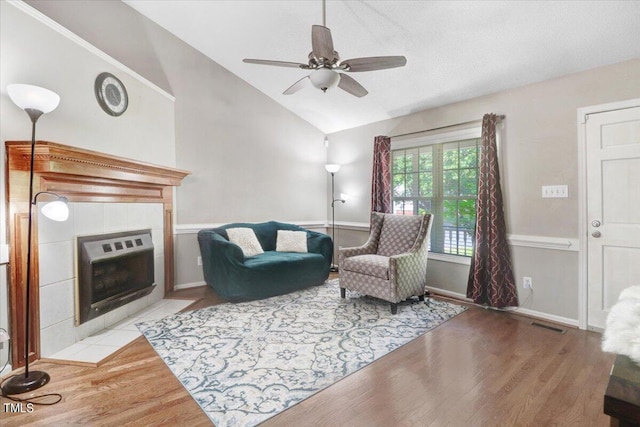 living room with hardwood / wood-style floors, ceiling fan, a tile fireplace, and vaulted ceiling