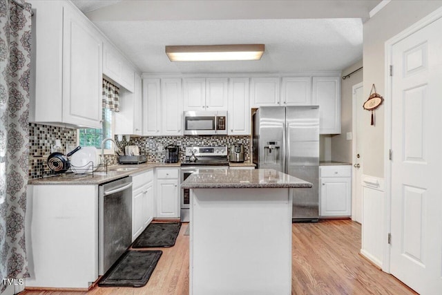 kitchen featuring appliances with stainless steel finishes, white cabinetry, a kitchen island, and light hardwood / wood-style flooring