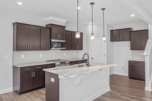 kitchen featuring sink, appliances with stainless steel finishes, an island with sink, decorative backsplash, and decorative light fixtures