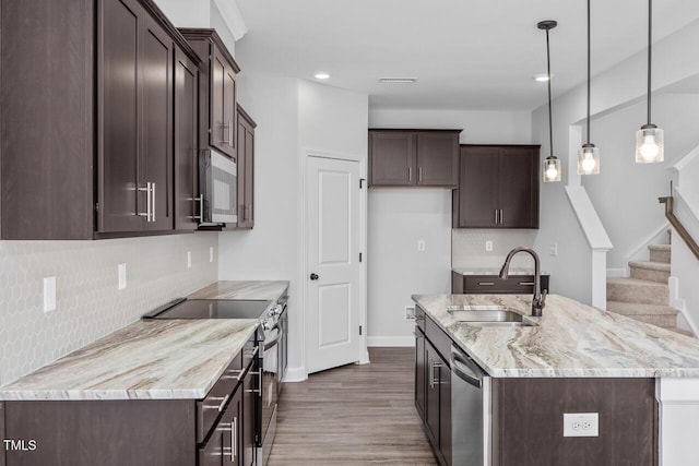 kitchen with sink, appliances with stainless steel finishes, light stone counters, an island with sink, and decorative light fixtures