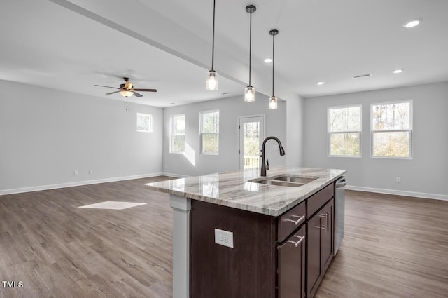 kitchen with an island with sink, sink, hanging light fixtures, stainless steel dishwasher, and light stone countertops