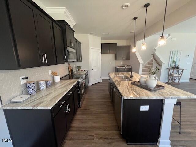 kitchen featuring pendant lighting, sink, a kitchen island with sink, stainless steel appliances, and light stone countertops