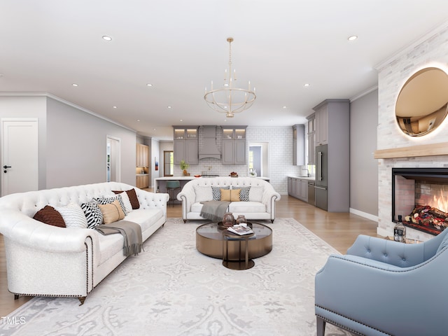 living room featuring ornamental molding, light wood-type flooring, an inviting chandelier, and a fireplace