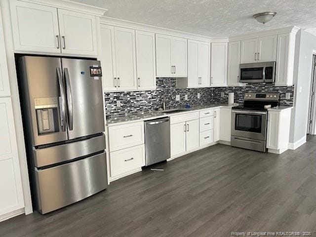 kitchen with appliances with stainless steel finishes, backsplash, sink, white cabinets, and dark hardwood / wood-style floors