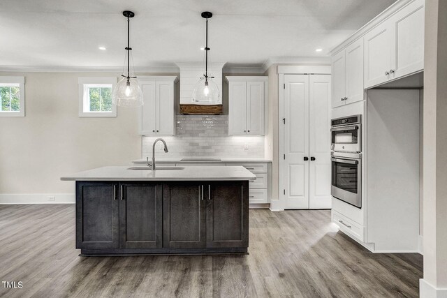 kitchen featuring decorative light fixtures, a kitchen island with sink, sink, and white cabinetry