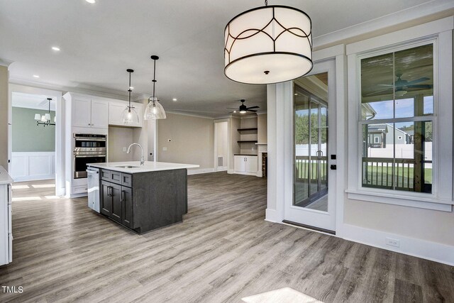 kitchen with pendant lighting, a center island with sink, white cabinetry, stainless steel double oven, and ceiling fan with notable chandelier