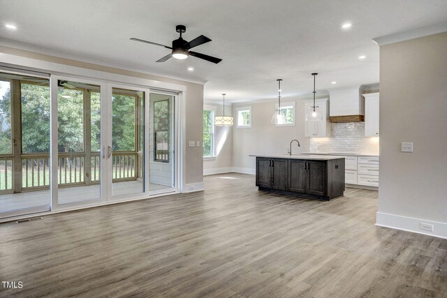 kitchen with ceiling fan, decorative light fixtures, a center island with sink, white cabinetry, and light wood-type flooring