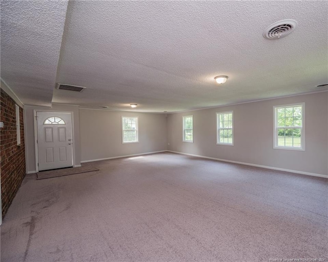 basement featuring a textured ceiling, light colored carpet, and brick wall