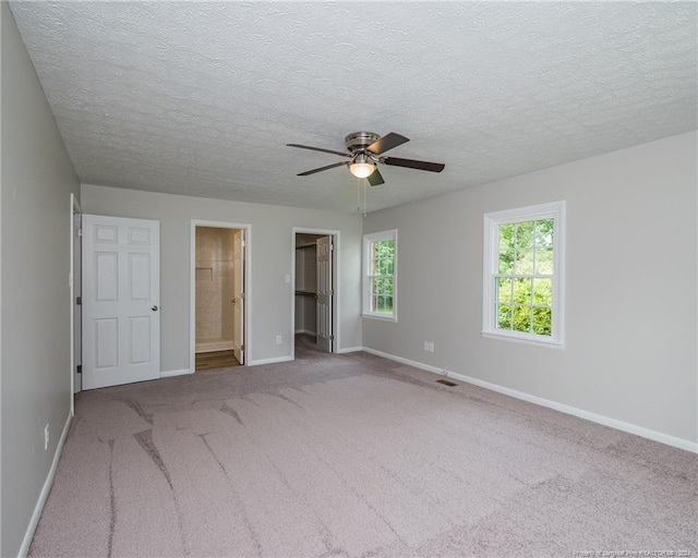 unfurnished bedroom with ensuite bathroom, ceiling fan, a spacious closet, light colored carpet, and a closet