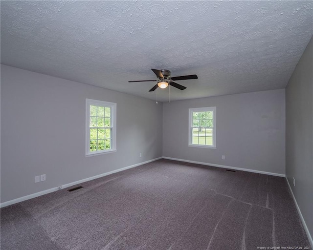 spare room with dark colored carpet, a textured ceiling, a wealth of natural light, and ceiling fan