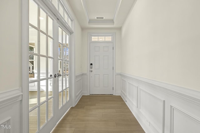 doorway to outside featuring crown molding, a raised ceiling, french doors, and light wood-type flooring