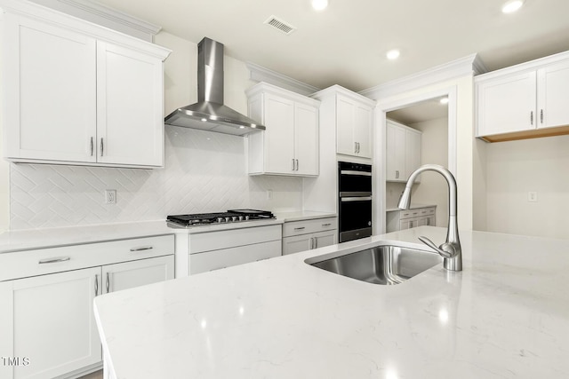 kitchen with sink, white cabinets, stainless steel gas cooktop, light stone countertops, and wall chimney exhaust hood