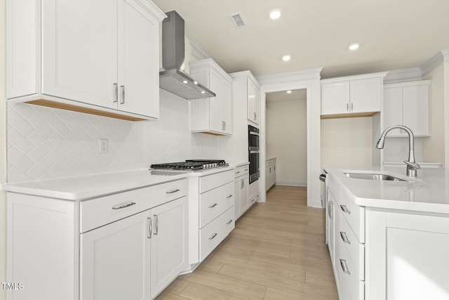 kitchen featuring sink, stainless steel gas cooktop, white cabinets, decorative backsplash, and wall chimney exhaust hood