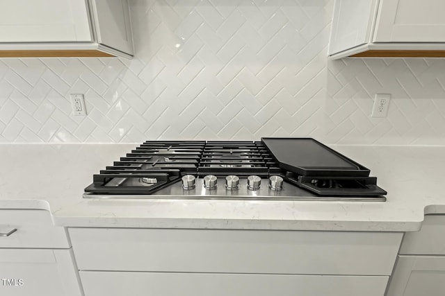 interior details with backsplash, stainless steel gas cooktop, light stone counters, and white cabinets