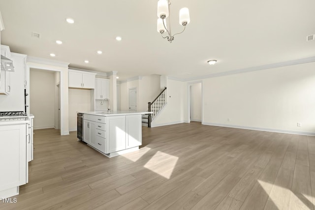 kitchen featuring sink, hanging light fixtures, light hardwood / wood-style floors, an island with sink, and white cabinets