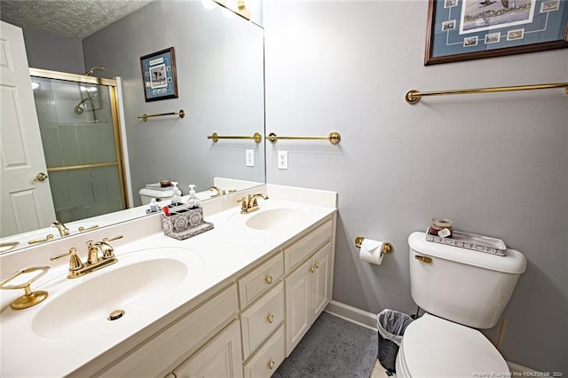 bathroom featuring vanity, toilet, a shower with door, and a textured ceiling