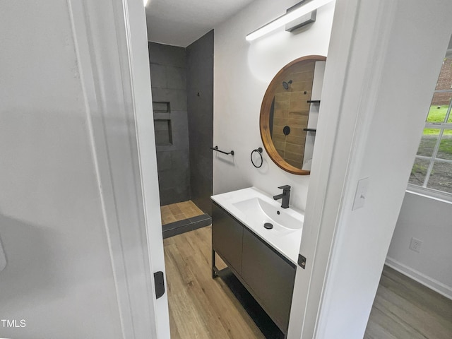 bathroom with tiled shower, hardwood / wood-style floors, and vanity