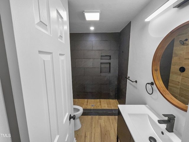 bathroom featuring a tile shower, toilet, vanity, and hardwood / wood-style flooring