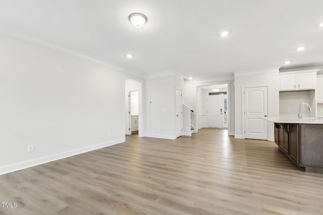 unfurnished living room with sink, ornamental molding, and light wood-type flooring