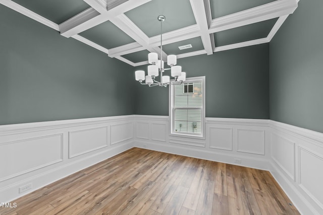 empty room featuring beam ceiling, light hardwood / wood-style flooring, coffered ceiling, and an inviting chandelier